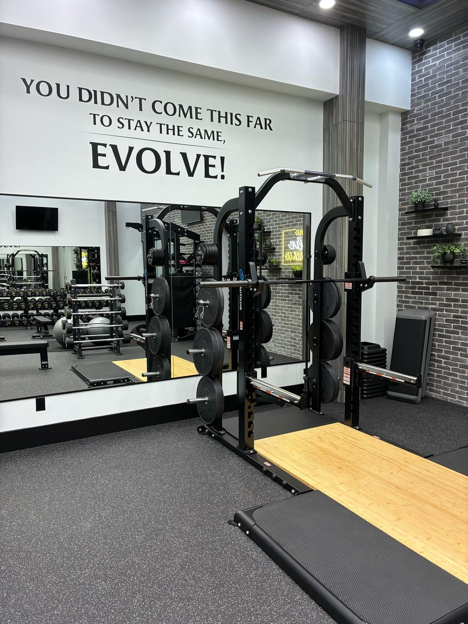 Squat rack and mirror wall beneath the Evolve motto